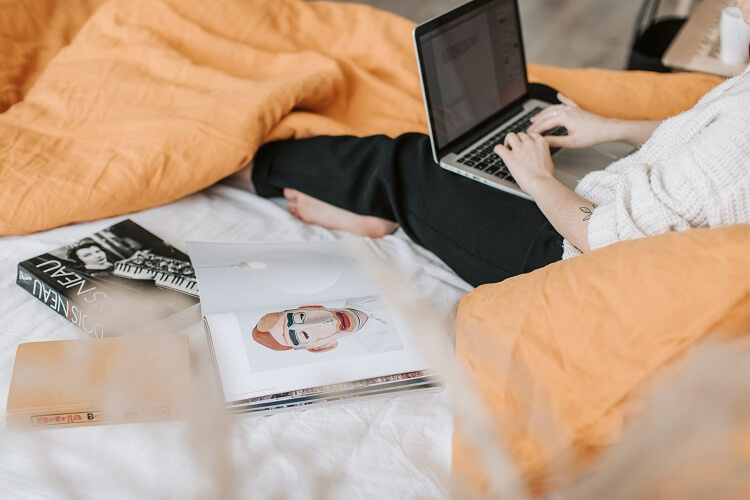 Ordinateur portable posé sur un lit avec un téléphone, un carnet et une tasse.