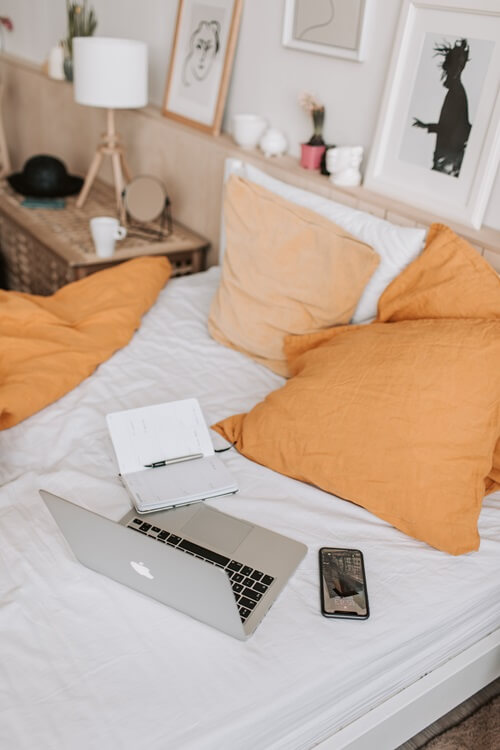 Ordinateur portable posé sur un lit avec un téléphone et un carnet.