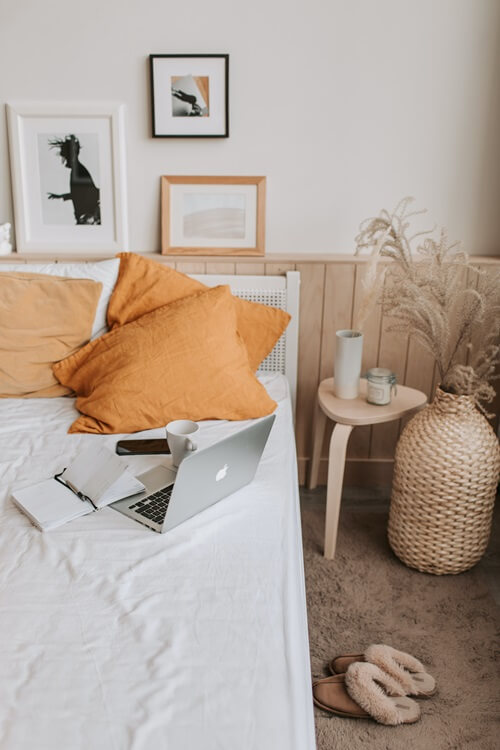 Ordinateur portable posé sur un lit avec un téléphone, un carnet et une tasse.